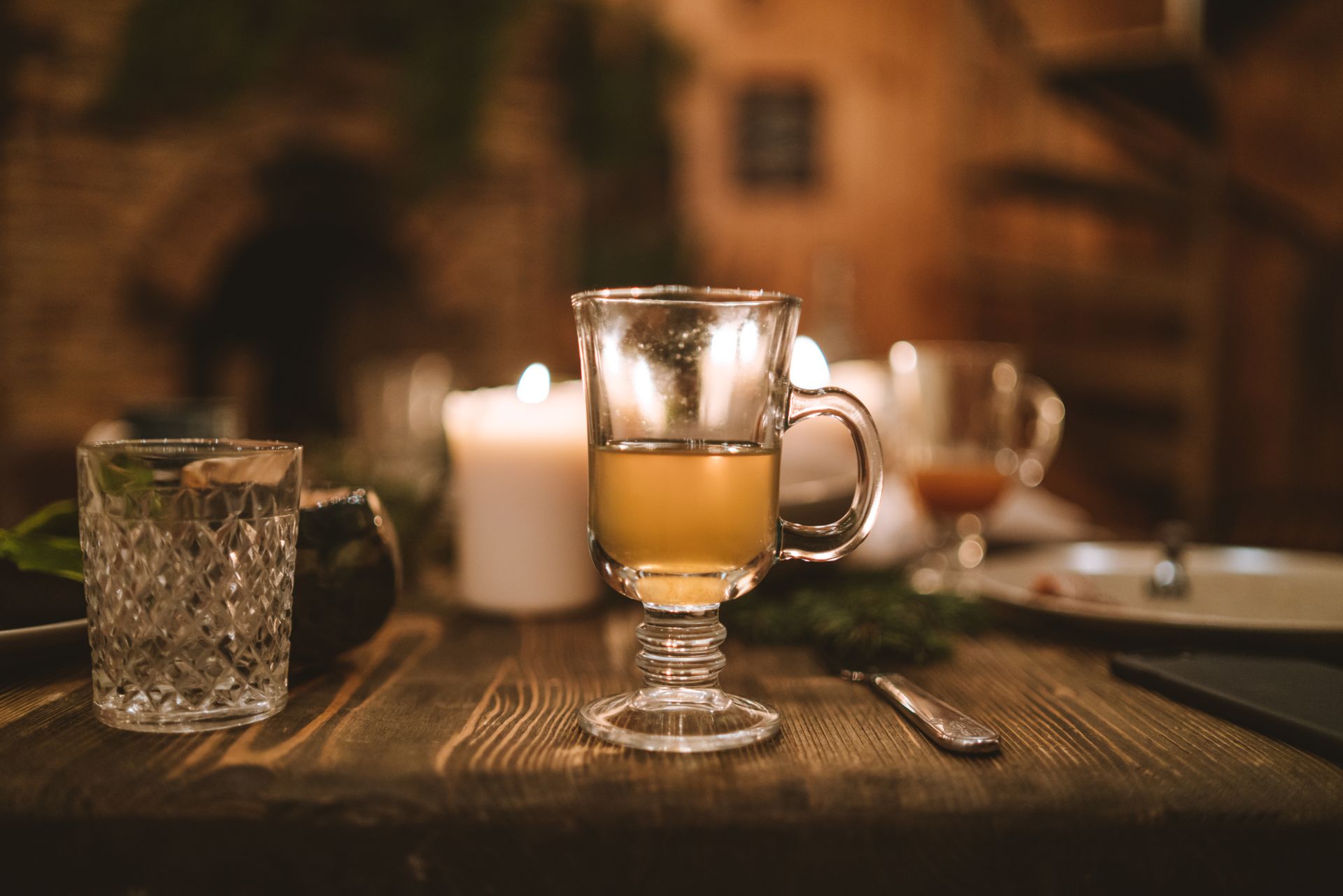 Dampfendes Heißgetränk im Glas auf einem rustikalen Holztisch mit Kerze als Sinnbild für gemütliche Weihnachtsmarkt-Atmosphäre