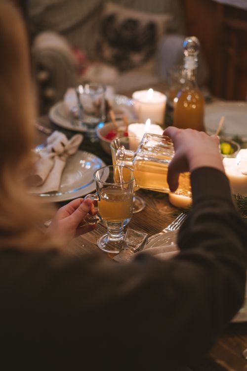 Free A warm indoor scene of a person pouring a beverage into a glass on a decorated dinner table. Stock Photo
