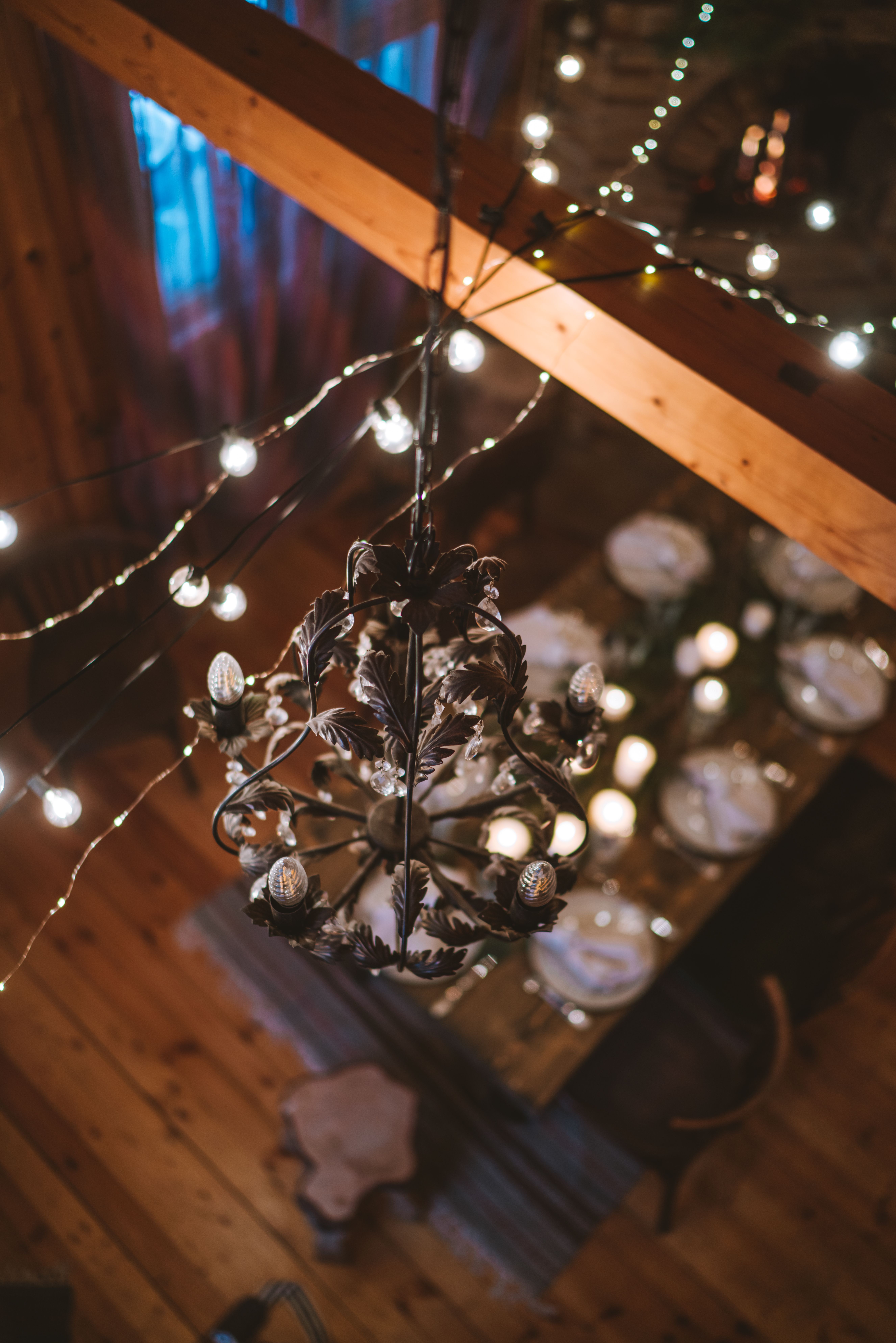 Layered lighting with chandelier and string lights over a dining table