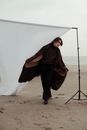 Man stylish clothes standing near fabric background placed on beach