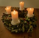 From above white thick candlesticks burning on creative wreath holder made of artificial plant leaves and placed on wooden table in dark room