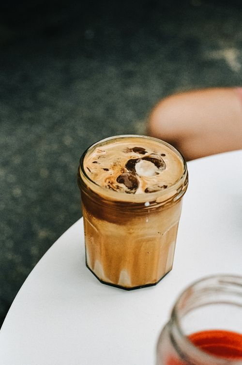 Free A delicious iced coffee in a jar with ice cubes on a white table outdoors. Stock Photo