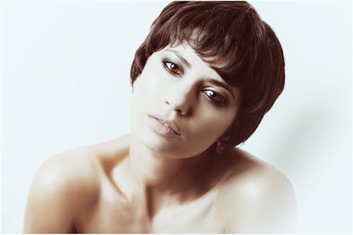 Sensual woman with bare shoulders looking at camera against light background