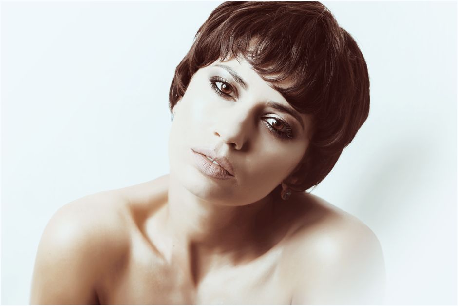 Naked woman with short dark hair and bright makeup looking at camera against light background