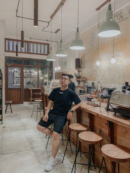 Man sitting on a stool in a modern café, surrounded by warm lighting and a relaxed atmosphere.