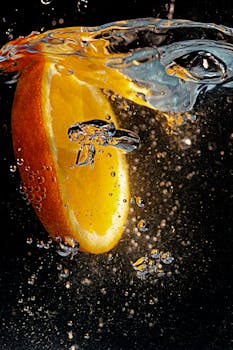 Orange slice splashes into water creating bubbles and vivid motion. Refreshing and vibrant.
