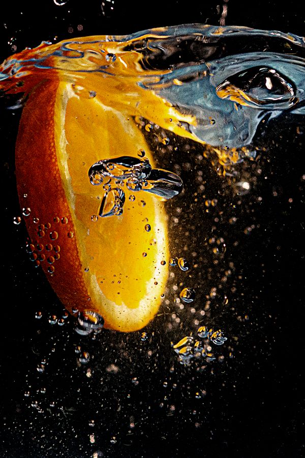 An orange slice splashing into water creating bubbles and motion