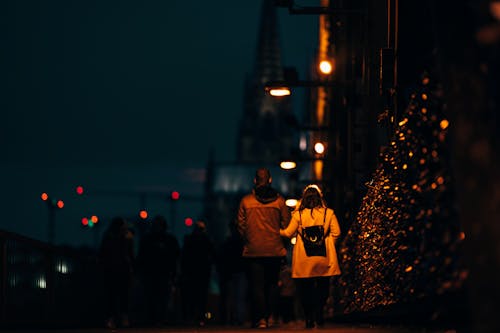 A Couple Walking On Sidewalk Of A Street During Night Time