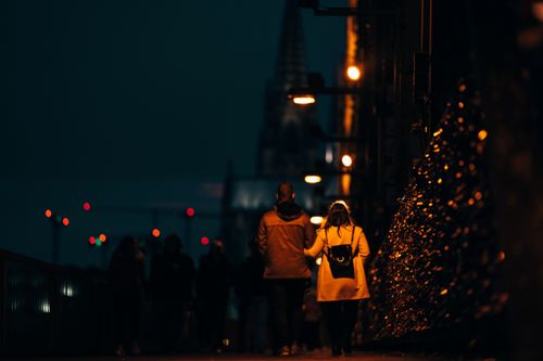 Free Couple walking on an illuminated street in Cologne at night, with the cathedral in view. Stock Photo