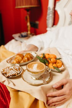 Indulge in a luxurious breakfast in bed featuring a latte, croissants, and fresh fruit on a tray.