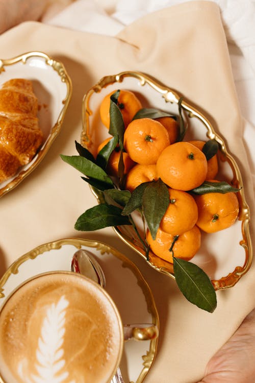 A Cup of Coffee on Ceramic Cup Beside Croissant and Oranges