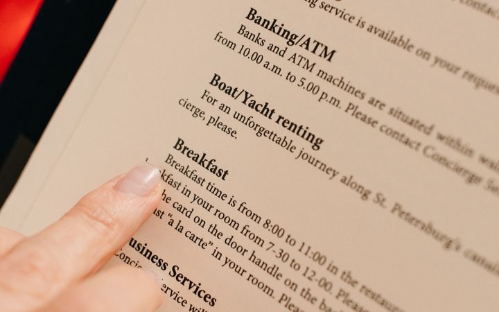 Close-up of a hand pointing at hotel service menu details on paper.