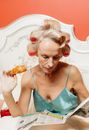 A Woman in a Nightgown Eating Croissant while Reading the Newspaper