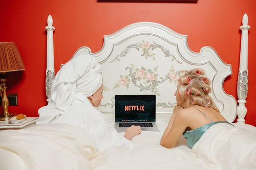 Free Two women lying in bed watching Netflix on a laptop, creating a cozy and bonding atmosphere. Stock Photo