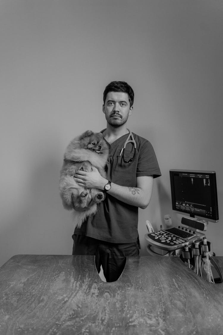 A Man In Scrubs Carrying A Dog 