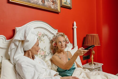 Women Sitting on the Bed While Watching TV