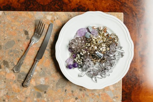 A plate filled with assorted jewelry alongside cutlery on a marble table.