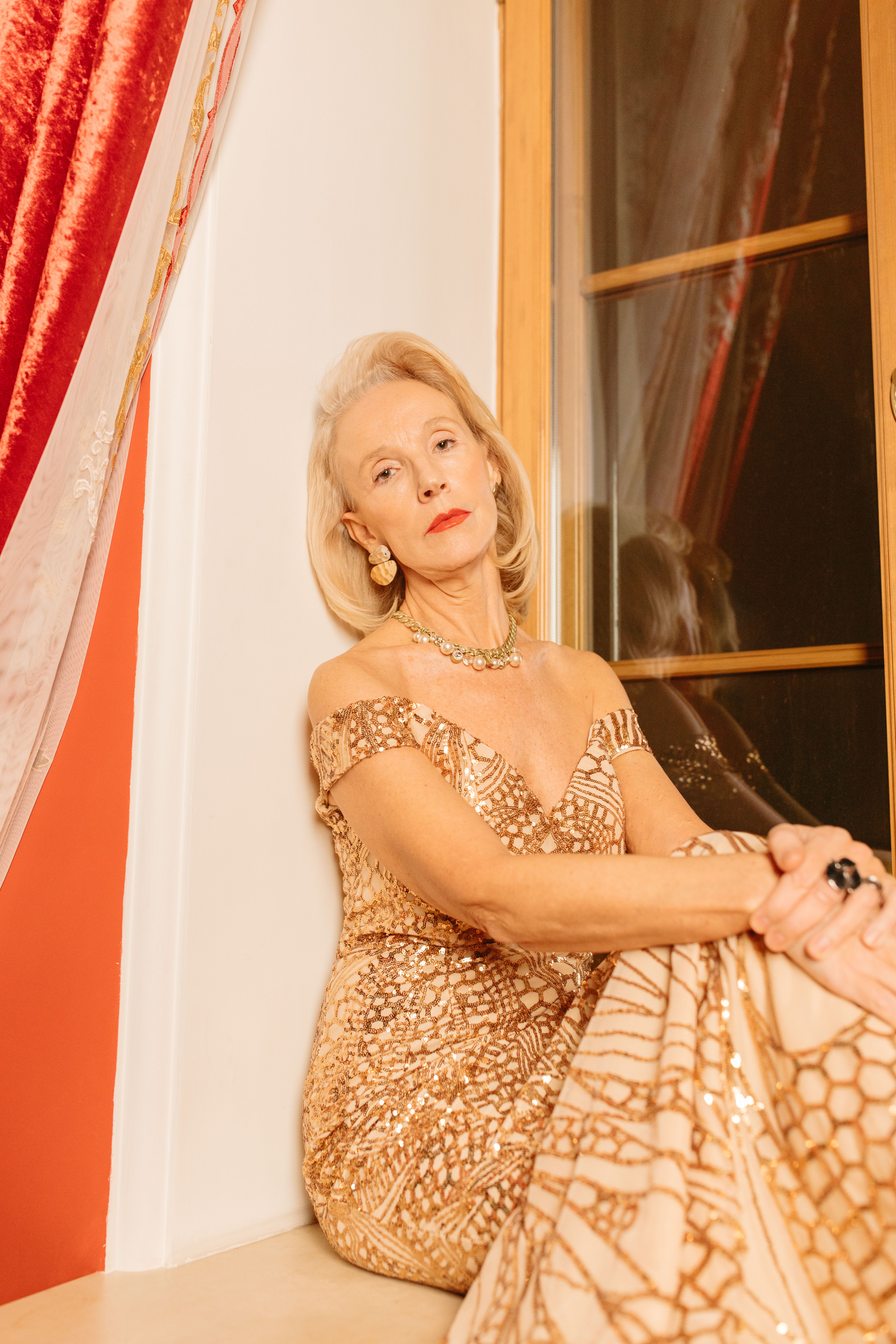 Sophisticated senior woman in elegant dress posing gracefully indoors by a window.