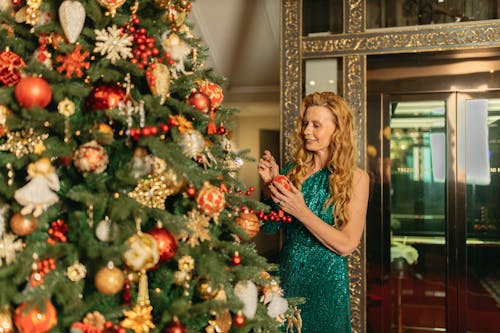 Woman in Green Sleeveless Dress Standing Beside Christmas Tree