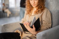 Young woman writing in notebook in comfortable armchair