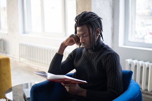 Young pensive black man with dreadlocks reading book