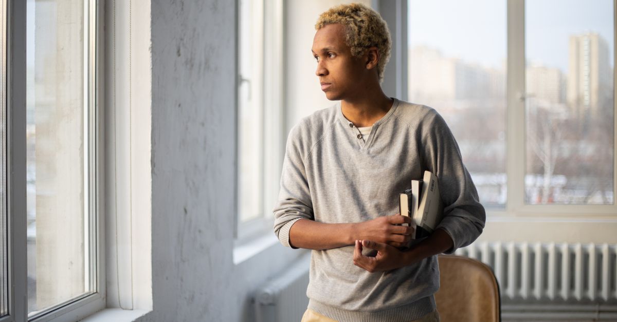 student looking away from textbook, staring out a window, relaxed posture