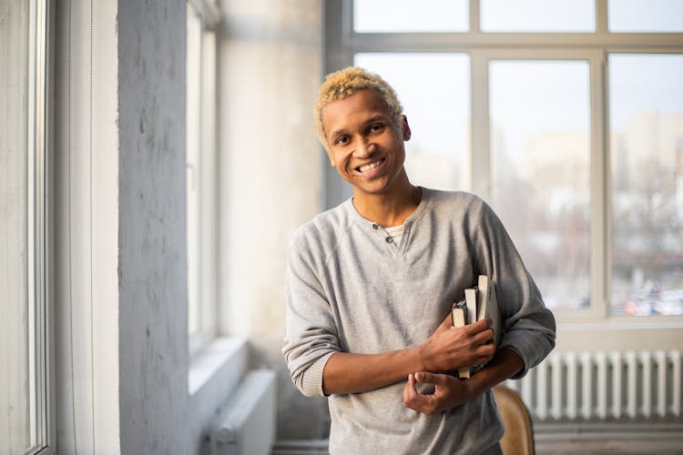 Smiling Black Man Standing With Books In Hand In Light Studio