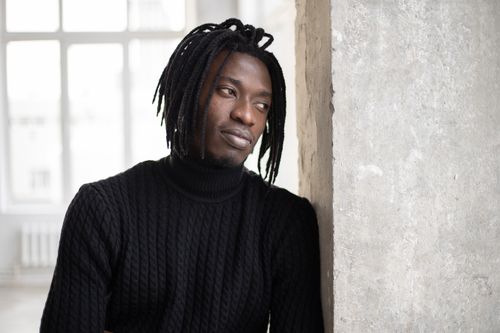 Free Calm black man with dreadlocks in casual sweater standing near concrete wall and pensively looking away in daytime Stock Photo