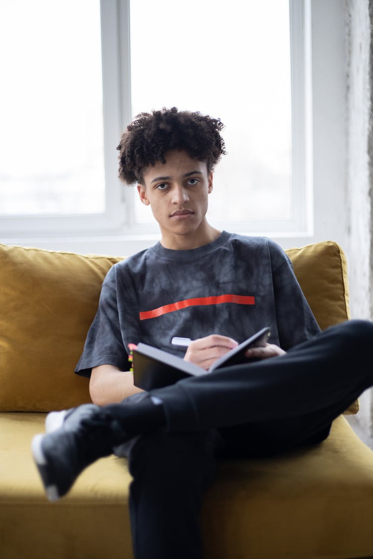 Serious Black Male Sitting On Couch And Taking Notes In Notebook