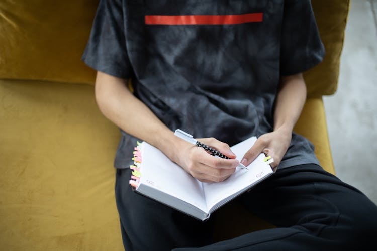 Crop Student Sitting On Couch And Taking Notes In Notebook