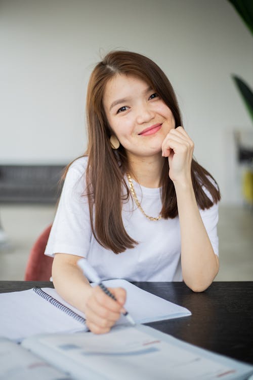 Cheerful Asian woman with pen studying in room