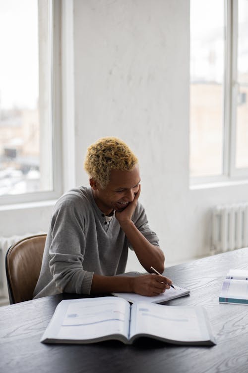 Cheerful black man writing in copybook