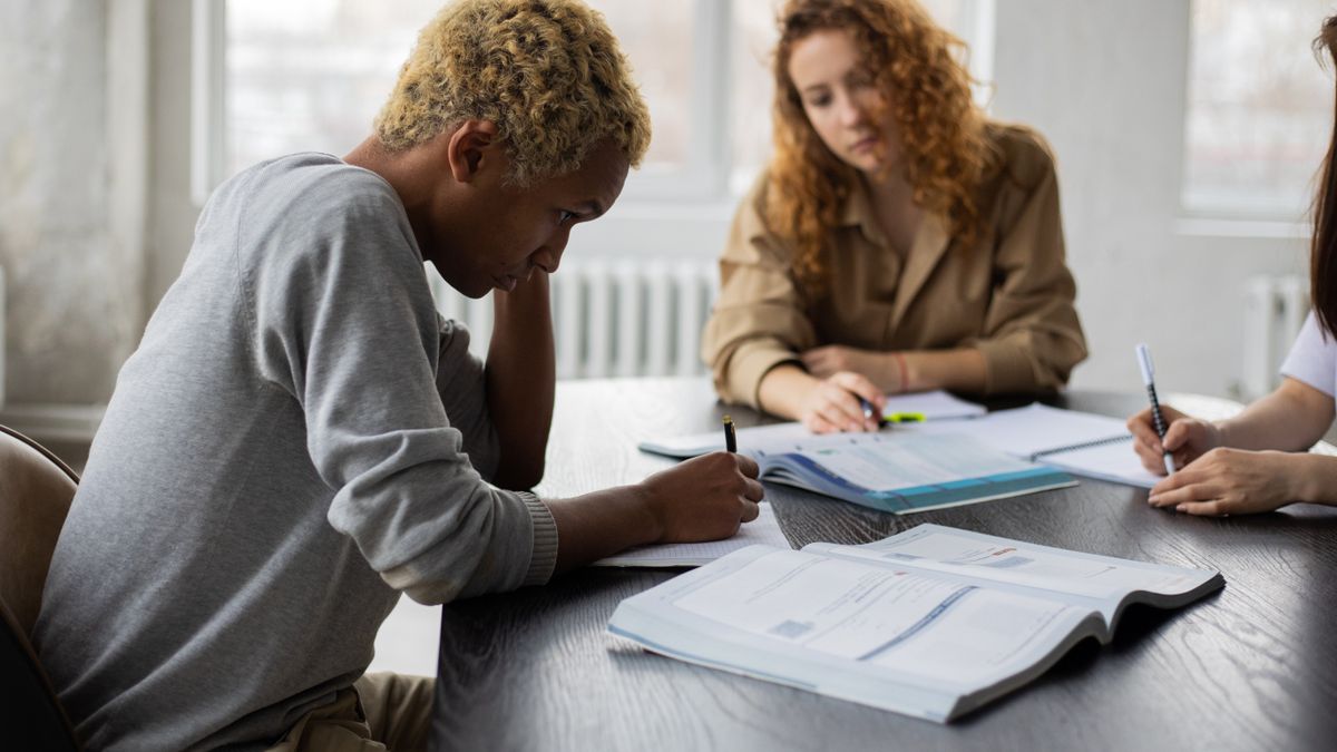 Grupo de estudantes adultos concentrados estudando juntos ao redor de uma mesa com cadernos e notebooks