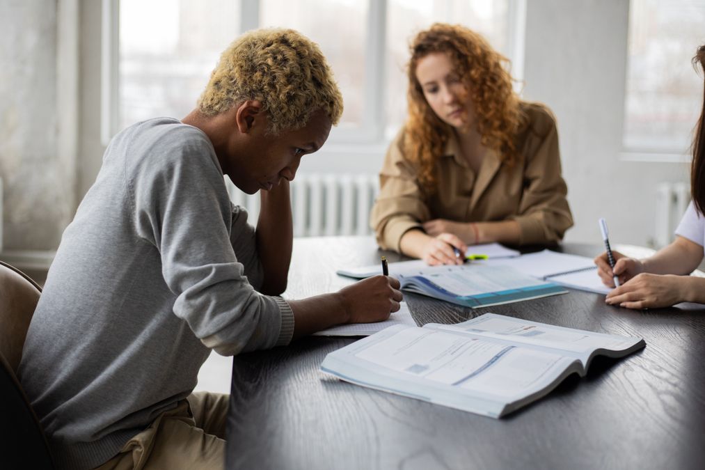 Grupo de estudantes adultos concentrados estudando juntos ao redor de uma mesa com cadernos e notebooks