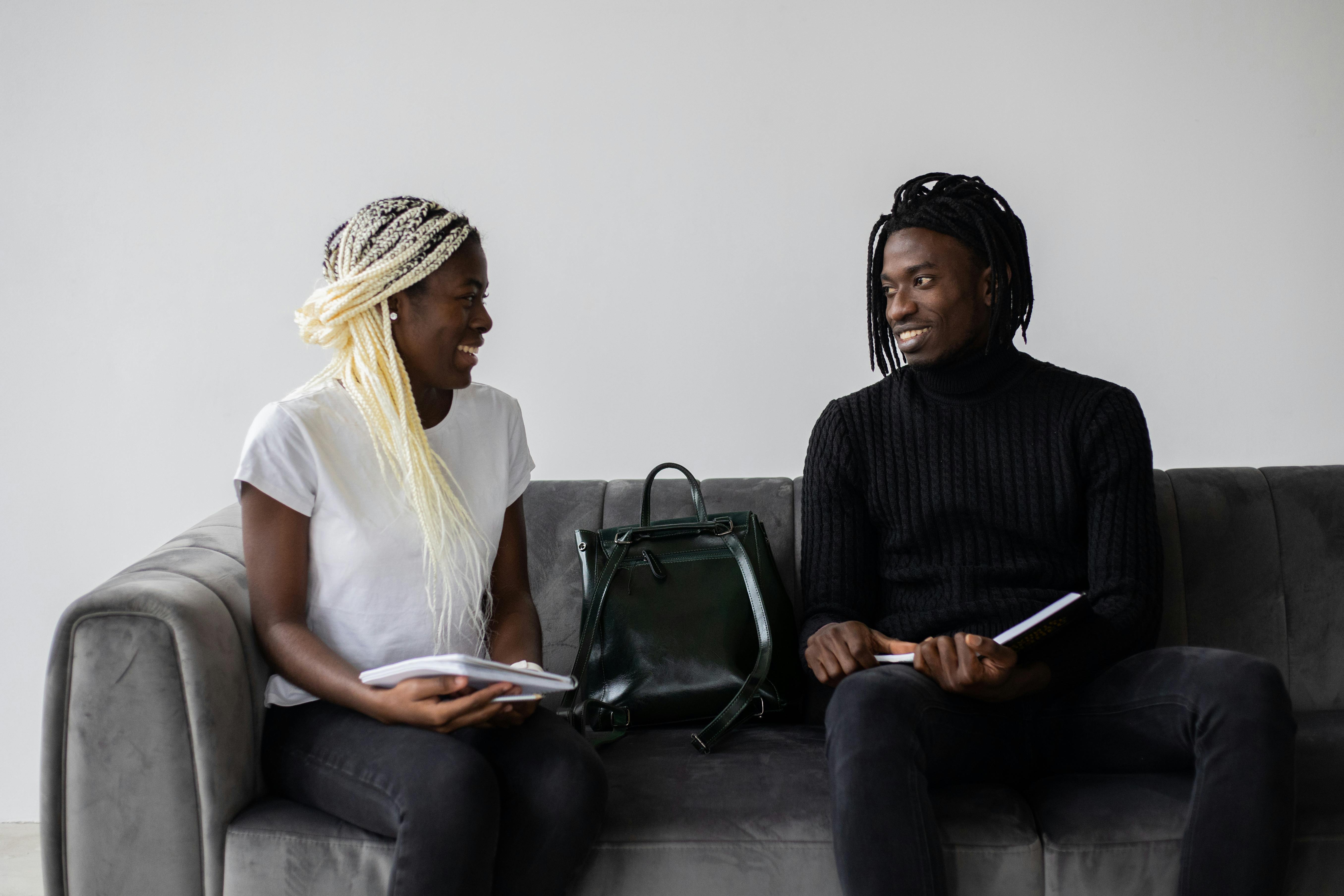 cheerful black students with copybooks chatting on sofa