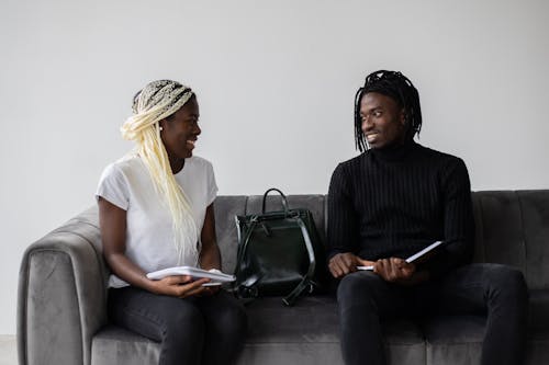 Cheerful black students with copybooks chatting on sofa