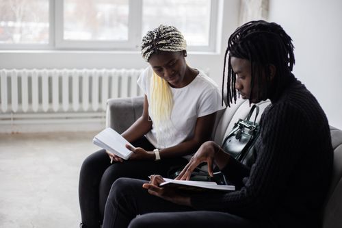 Free Serious African American classmates looking at notes in notebooks and sitting on sofa while preparing for exam in light room Stock Photo