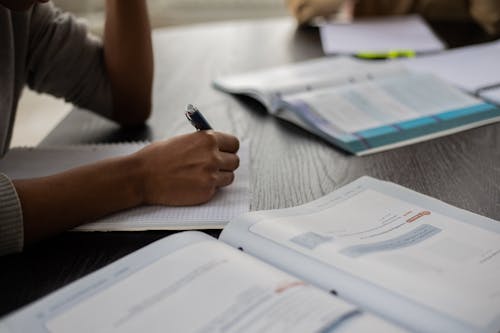 Crop black person writing in workbook while studying