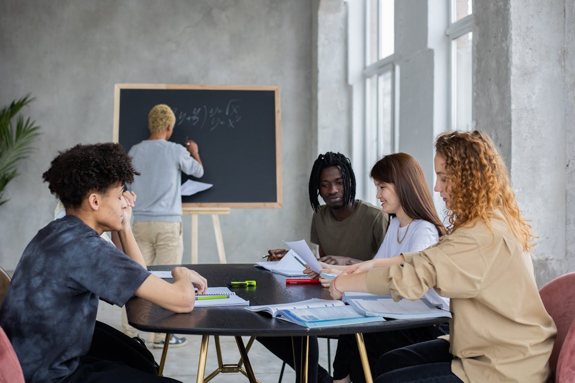 Free Unrecognizable male writing mathematical equation on chalkboard in classroom with group of multiethnic student at table solving task during lesson Stock Photo