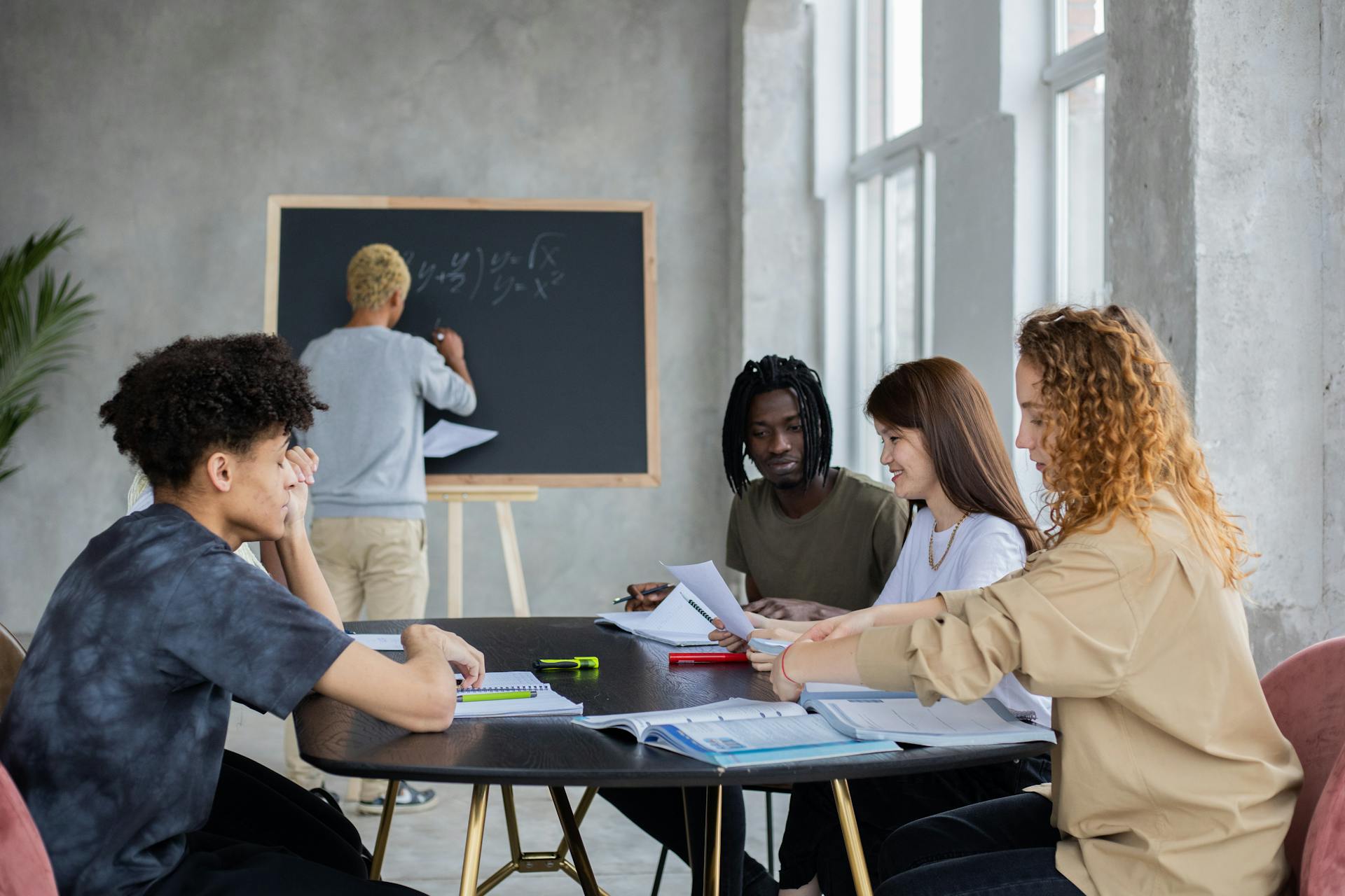 Unrecognizable male writing mathematical equation on chalkboard in classroom with group of multiethnic student at table solving task during lesson