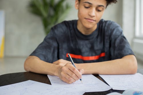 Free Crop African American male student taking notes on piece of paper at table while studying subject in classroom on blurred background Stock Photo