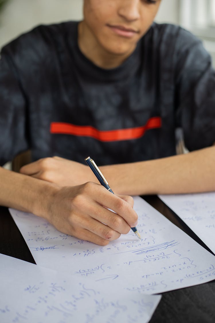 Crop Black Man Writing On Paper In Classroom