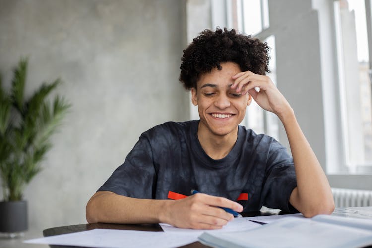 Cheerful Black Man Writing On Paper