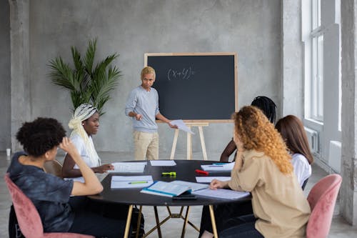 Free African American student explaining mathematic equation to diverse classmates while doing homework together in spacious room Stock Photo