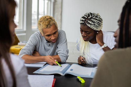Free A group of diverse students collaborate on a study assignment indoors, focusing on textbooks. Stock Photo