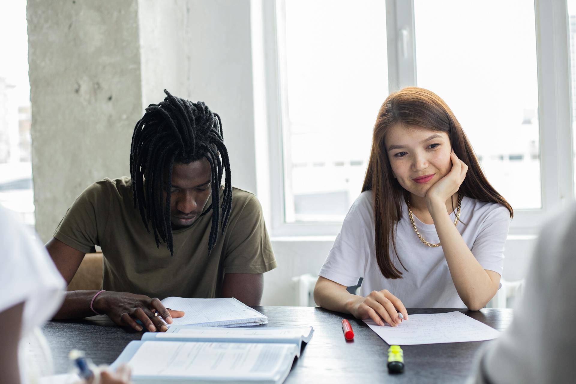 Multiethnic group of classmates sitting at table with notebook and textbook while studying together in university