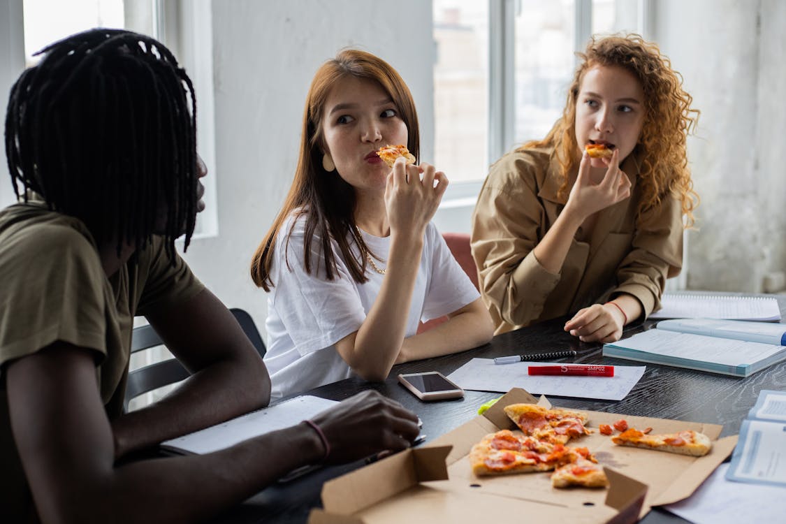 Free Multiethnic students eating pizza during break in studies Stock Photo