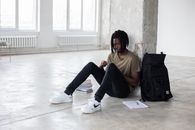 Full body of upset African American man sitting among textbooks and notebook near backpack during break in exam preparation