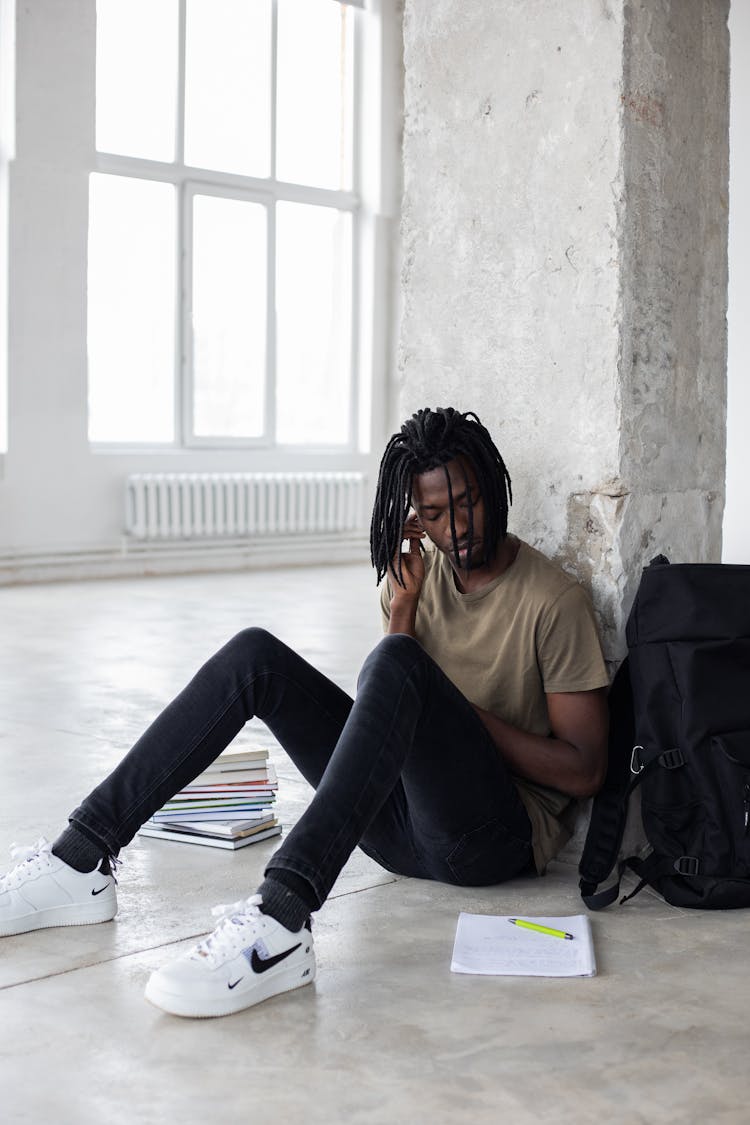 Black Student Sitting Near Concrete Column With Notebook