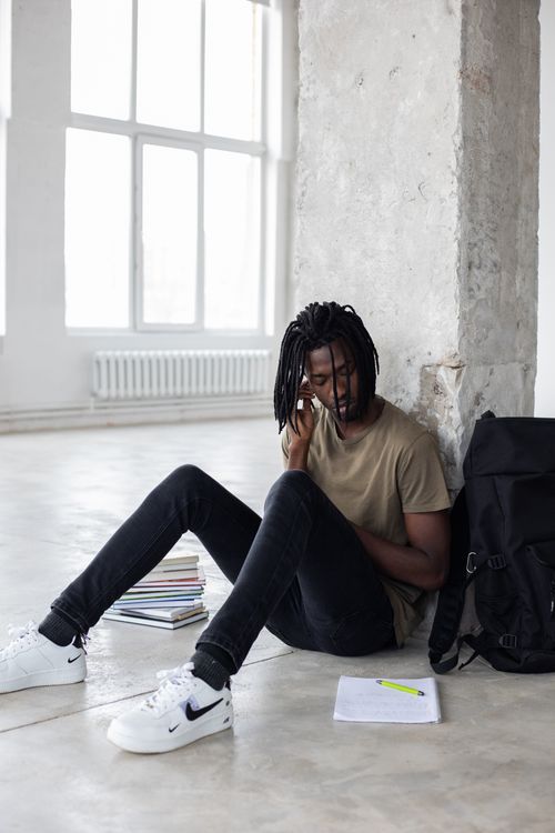 Free Full body of African American male learner sitting on floor with textbooks and notebook during studies Stock Photo